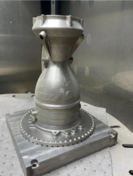 The Inconel chamber standing on its build plate straight off the printer, rough grey surface and bolt ring at the base