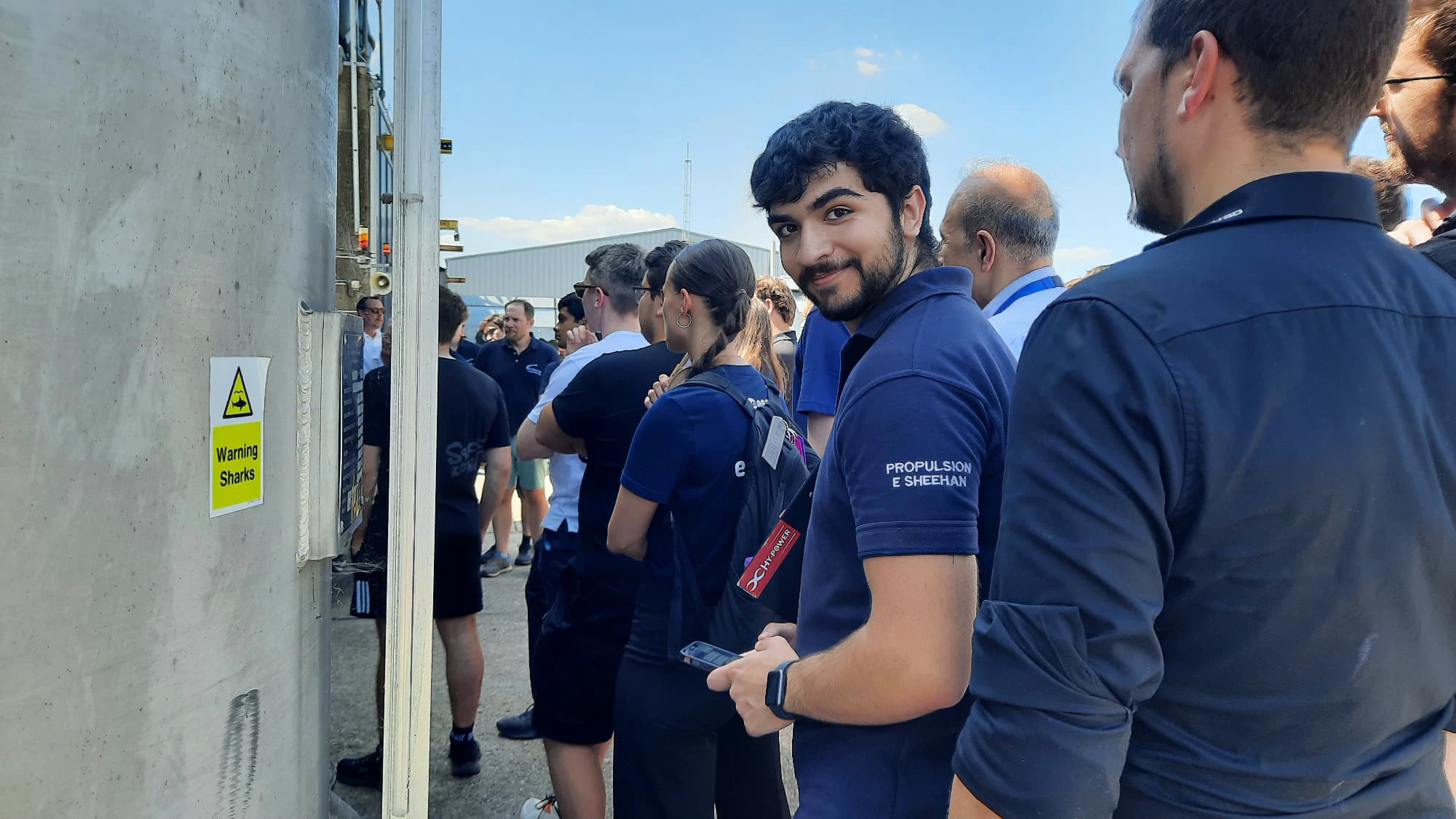 Candid photo of Ethan at the Airborne Engineering site beside a Warning Sharks sign