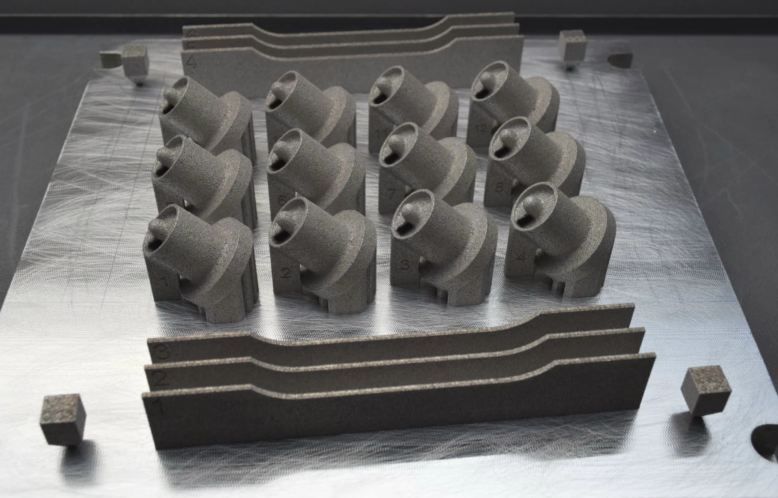 Build plate carrying small coaxial-swirl element test prints alongside tensile bars