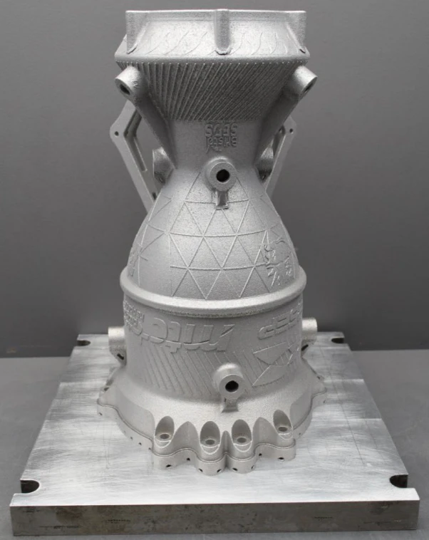 As-printed aluminium chamber standing inverted on its build plate with a printed support strut behind and BSEP and MTC marks embossed in the skin