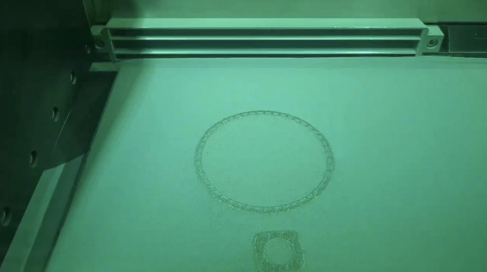 Build-camera frame from an earlier layer showing the ring of the chamber wall and a support cross-section in the powder