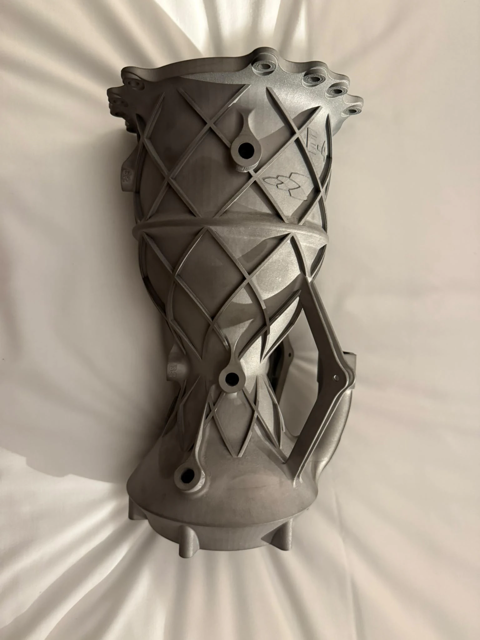 The printed Inconel 718 chamber standing upright with its isogrid lattice, E-4 and snowflake embossing and brace webs still attached