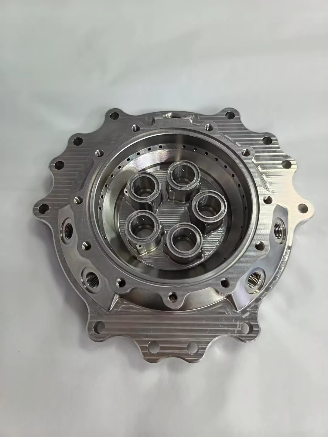 Injector body face-on with five element bores standing in a counterbore and a ring of small drilled ports on the shoulder