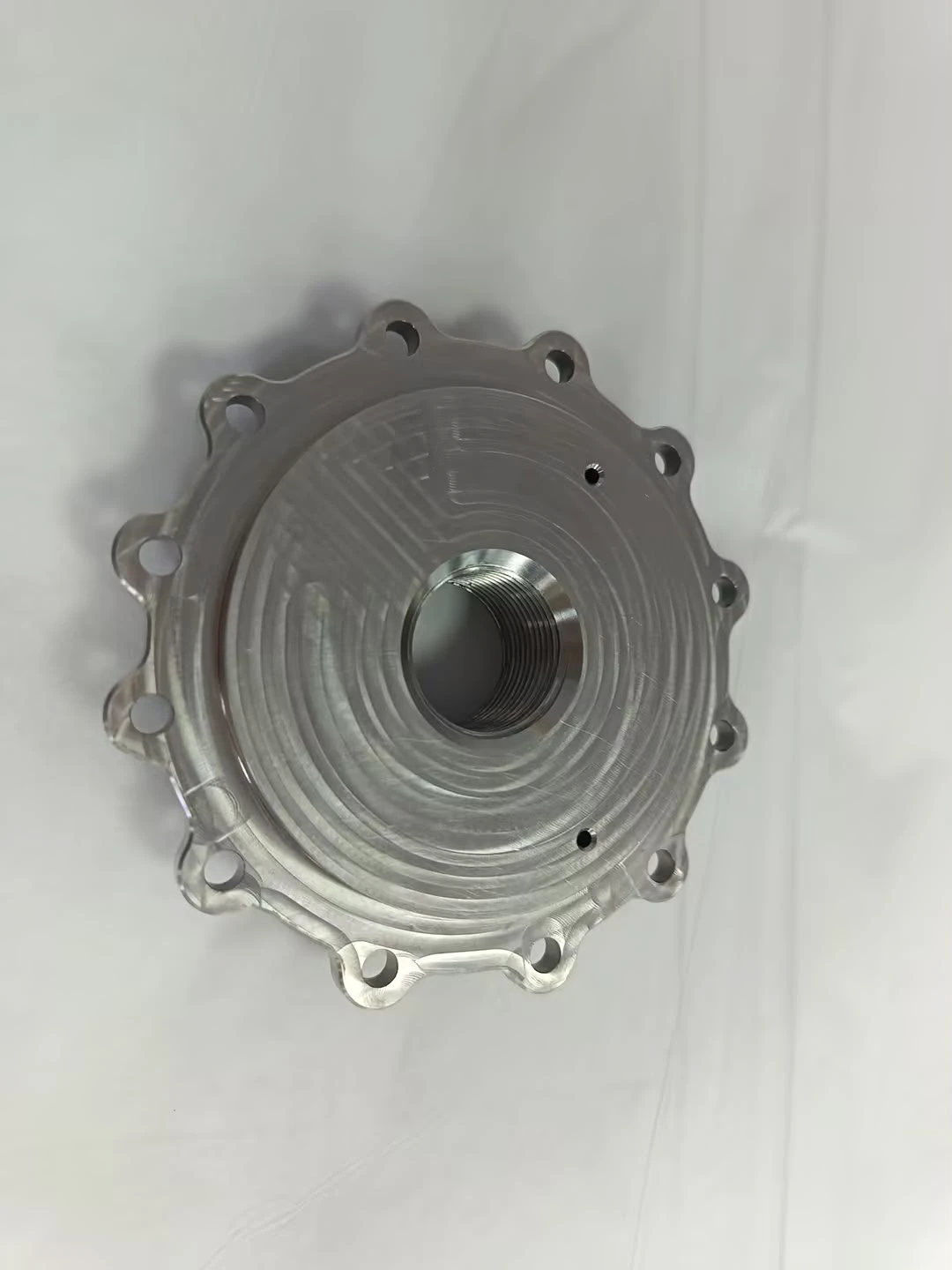 Machined plate with a central threaded port and a fine spiral finish across its face