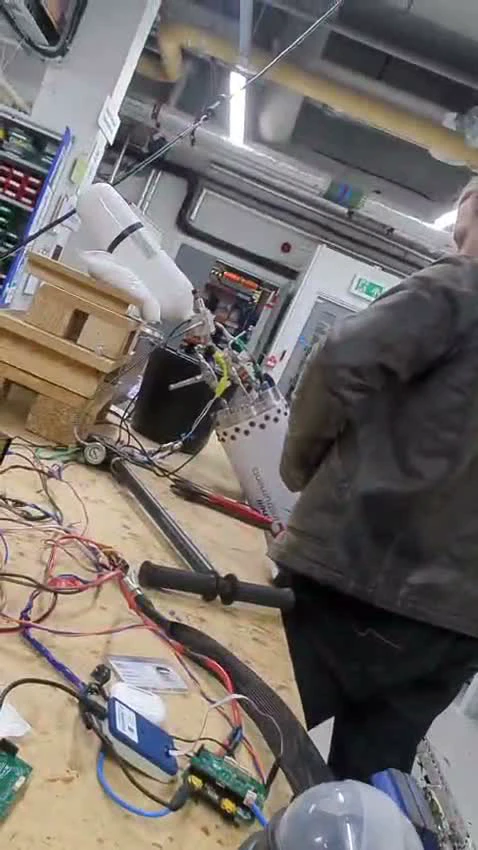 The bench rig in the workshop: a pressure vessel and pipework on a wooden stand, STM32 boards and wiring on the table, a team member at the bench
