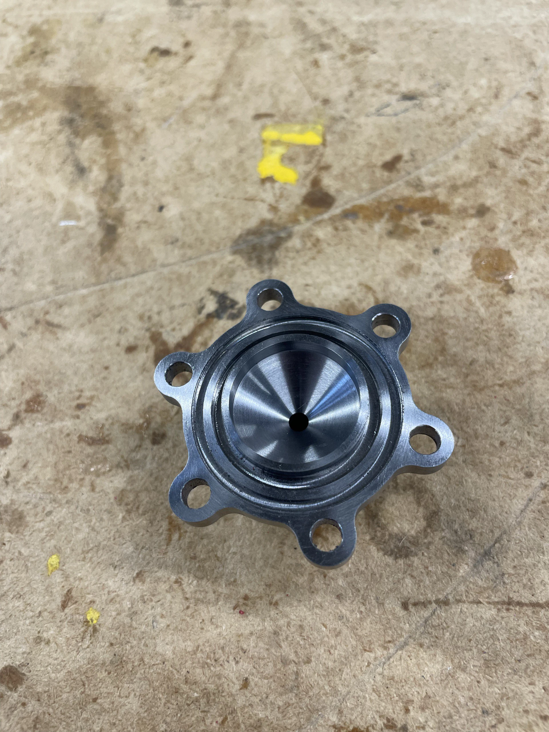 Machined steel chamber cap on a bench, its concave internal face and central port catching the light.