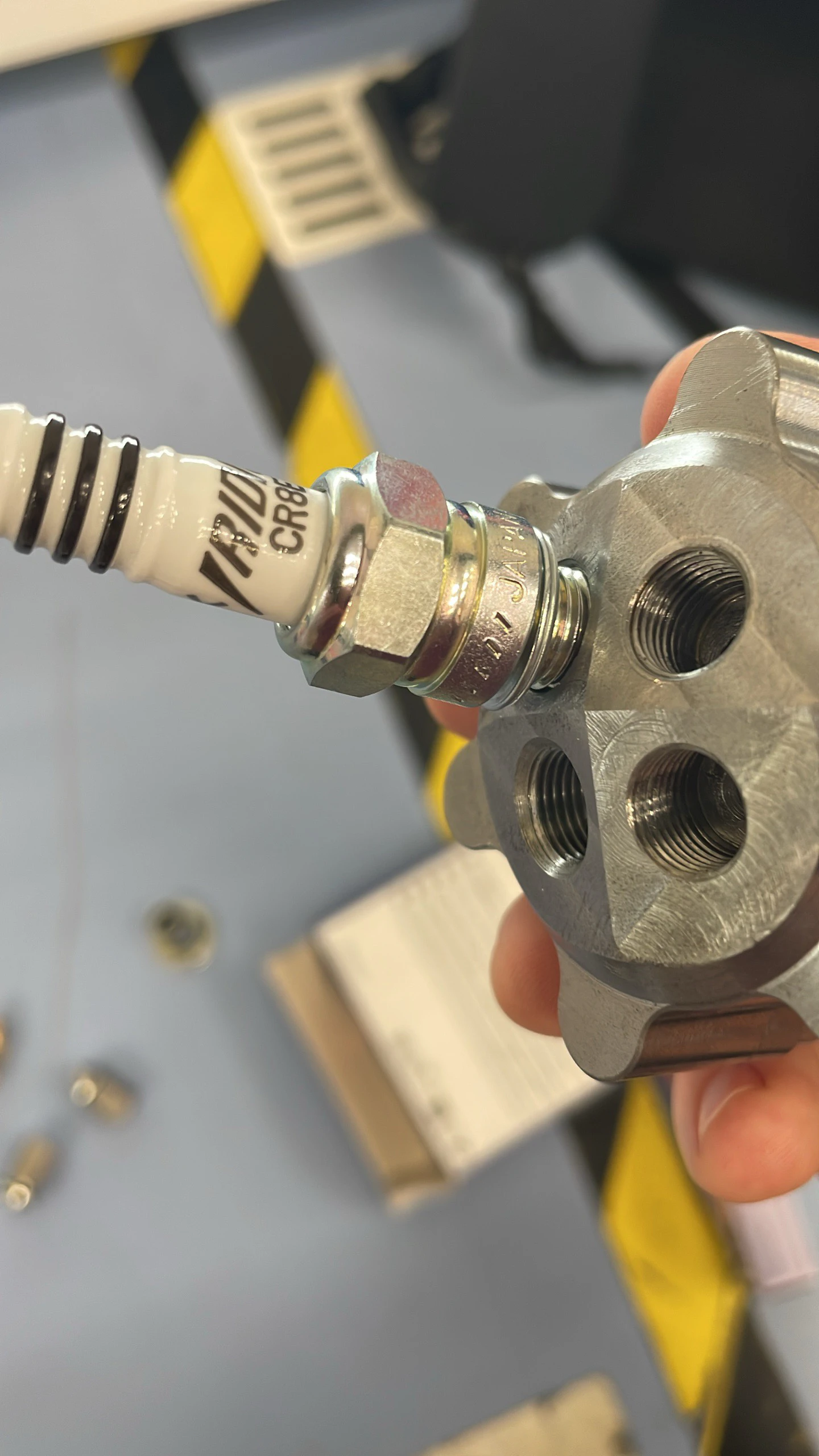 Hands threading a brass inlet fitting into the steel igniter body, spark plug already installed.