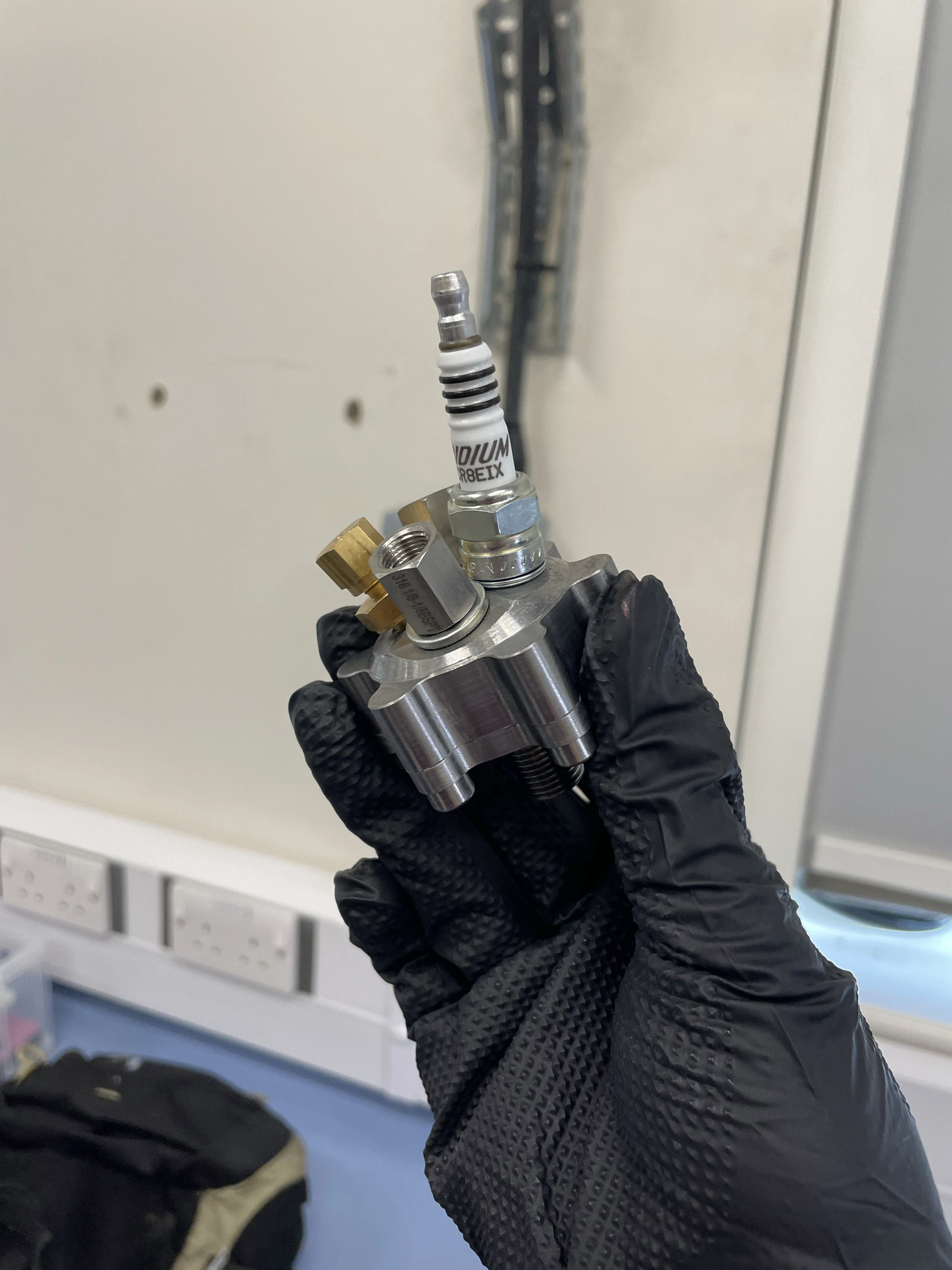 The assembled steel igniter, spark plug and brass fittings included, held in one black-gloved hand.