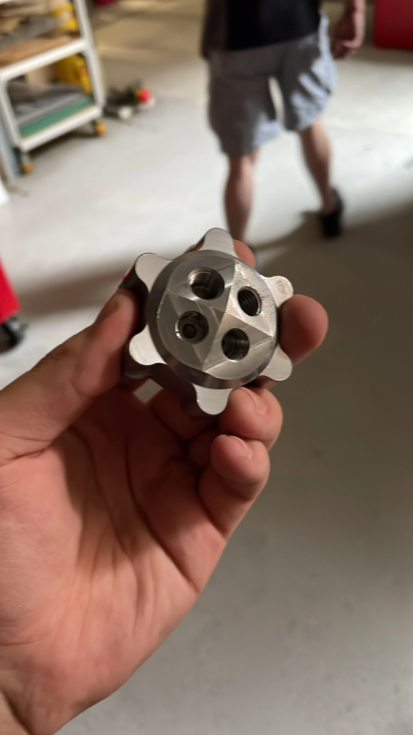 A hand holding the freshly machined injector half, two small impinging-jet ports visible in the face.