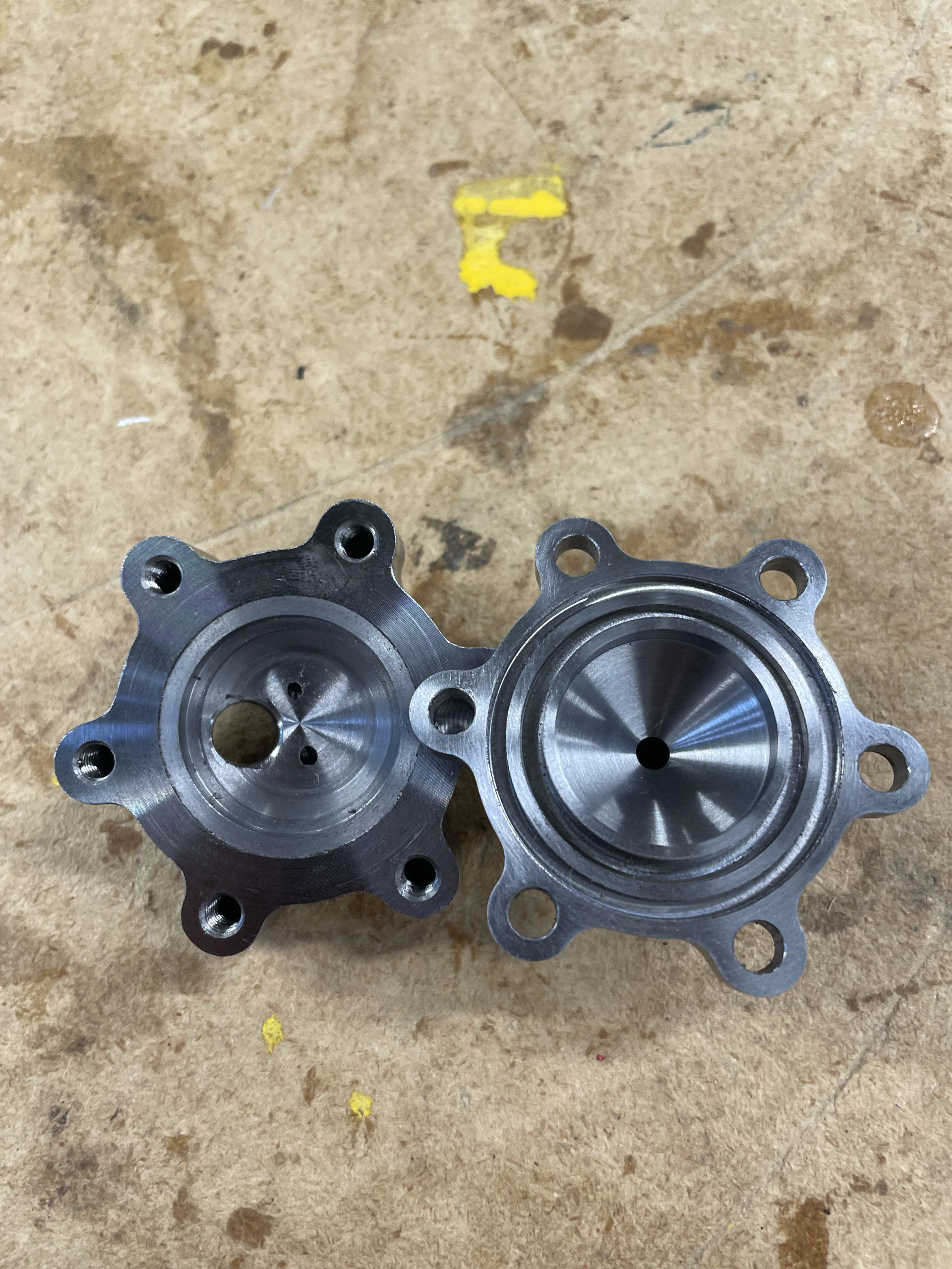 Both machined steel halves of the igniter lying face-up side by side on a workshop bench.