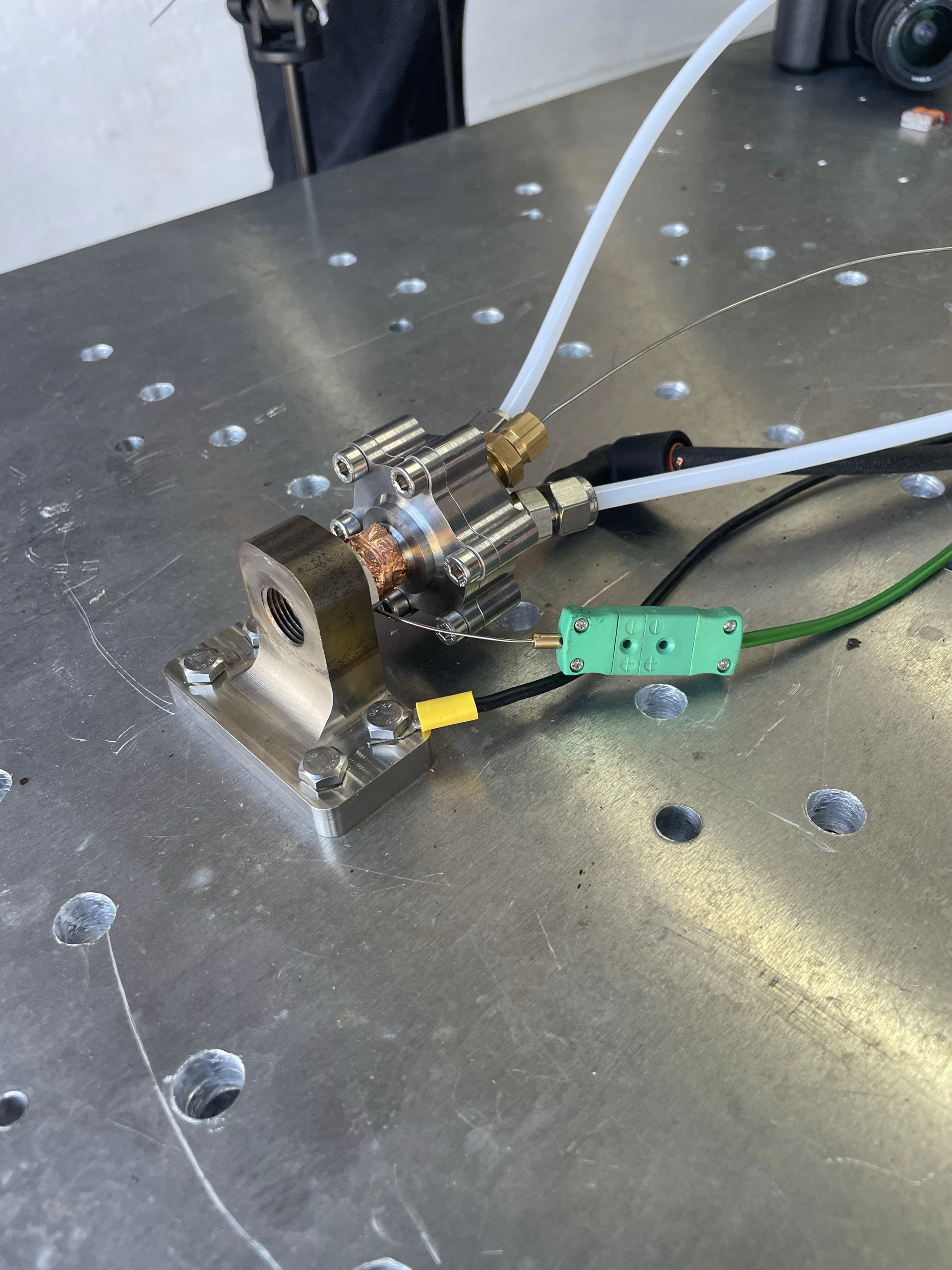 The igniter bolted to a steel bracket on a perforated test plate, thermocouple wires taped to the body.