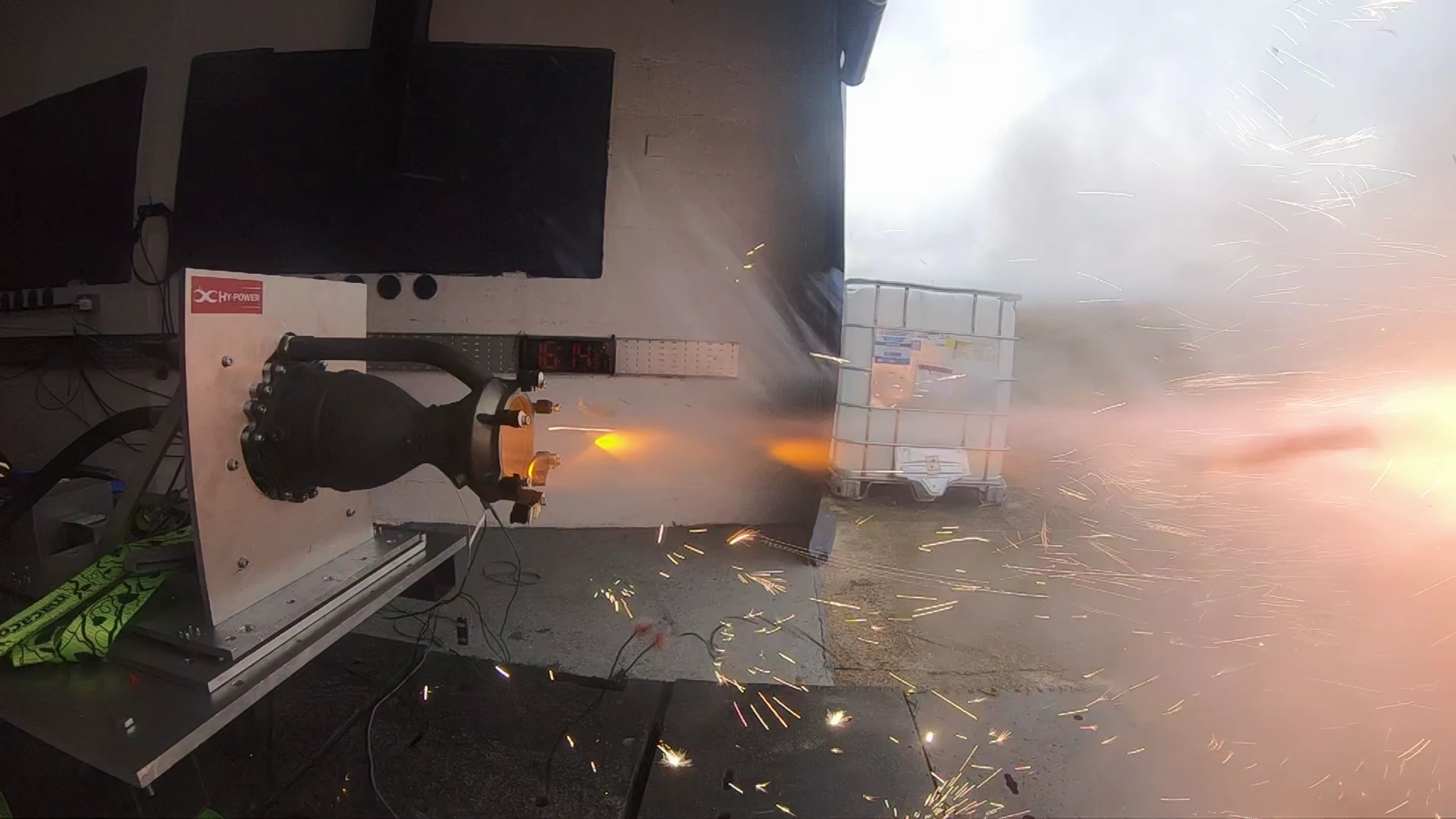 Hotfire 1 just after ignition, a short orange plume forming while sparks scatter across the pad below the engine