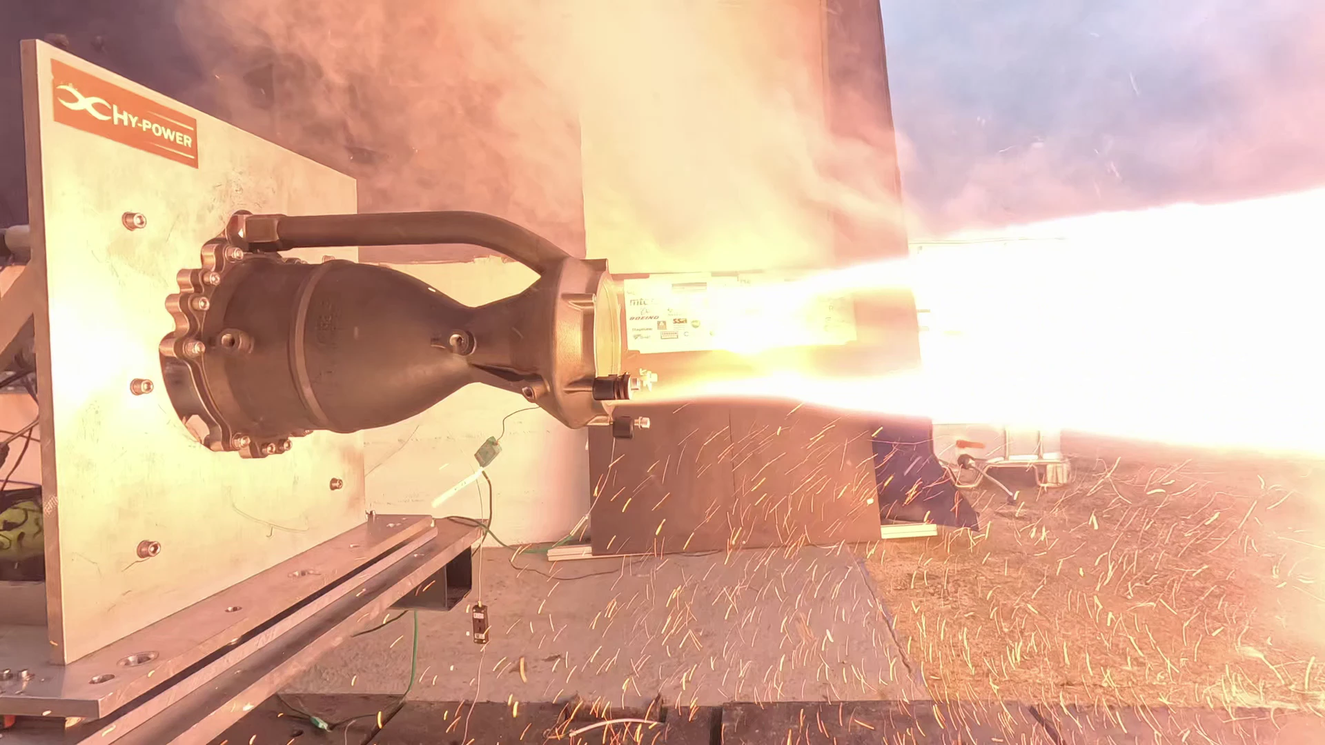 Ignition of Hotfire 2: a burst of sparks and flame at the nozzle exit with embers scattered across the pad