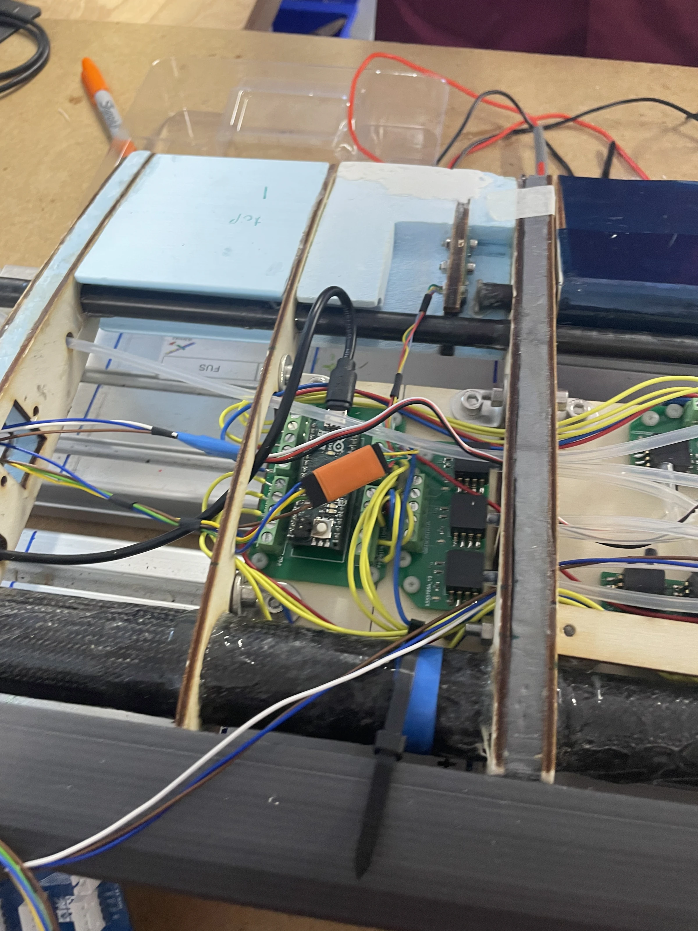 A green Hall-effect sensor board bolted to a plywood rib inside the wing structure, wired out through the bay alongside the carbon spar
