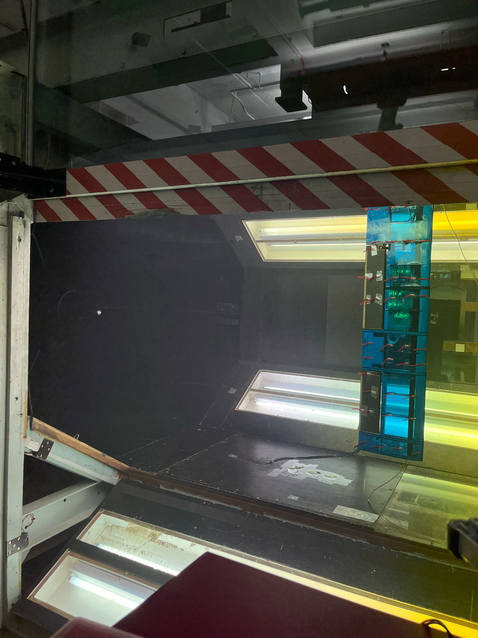 The wind tunnel test section from outside, the blue wing standing vertically inside behind yellow-tinted glass