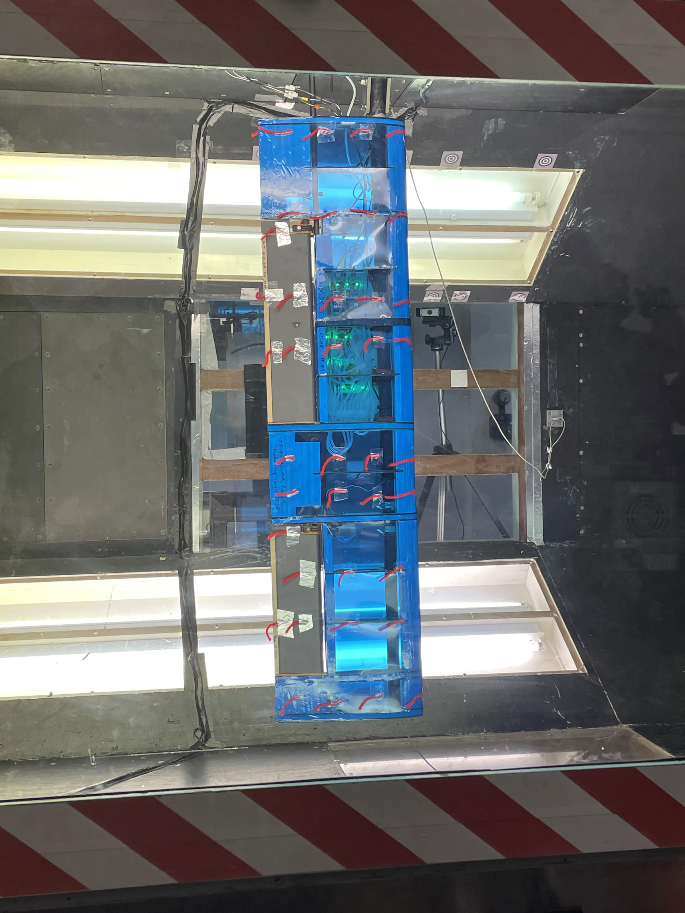 The wing installed vertically in the wind tunnel, seen from above through the ceiling window, tufts and sensor LEDs visible