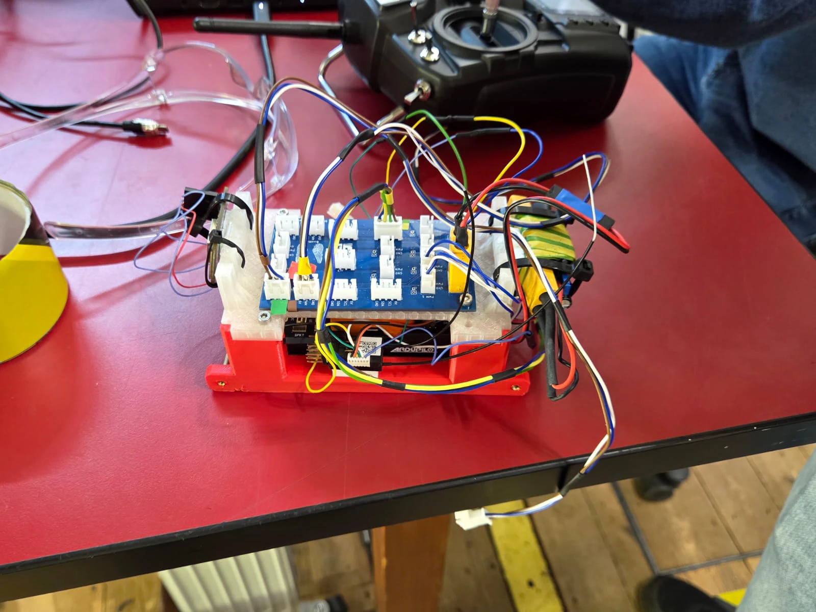 A red 3D-printed tray holding a blue terminal board with many coloured wires, next to a radio transmitter on a red bench