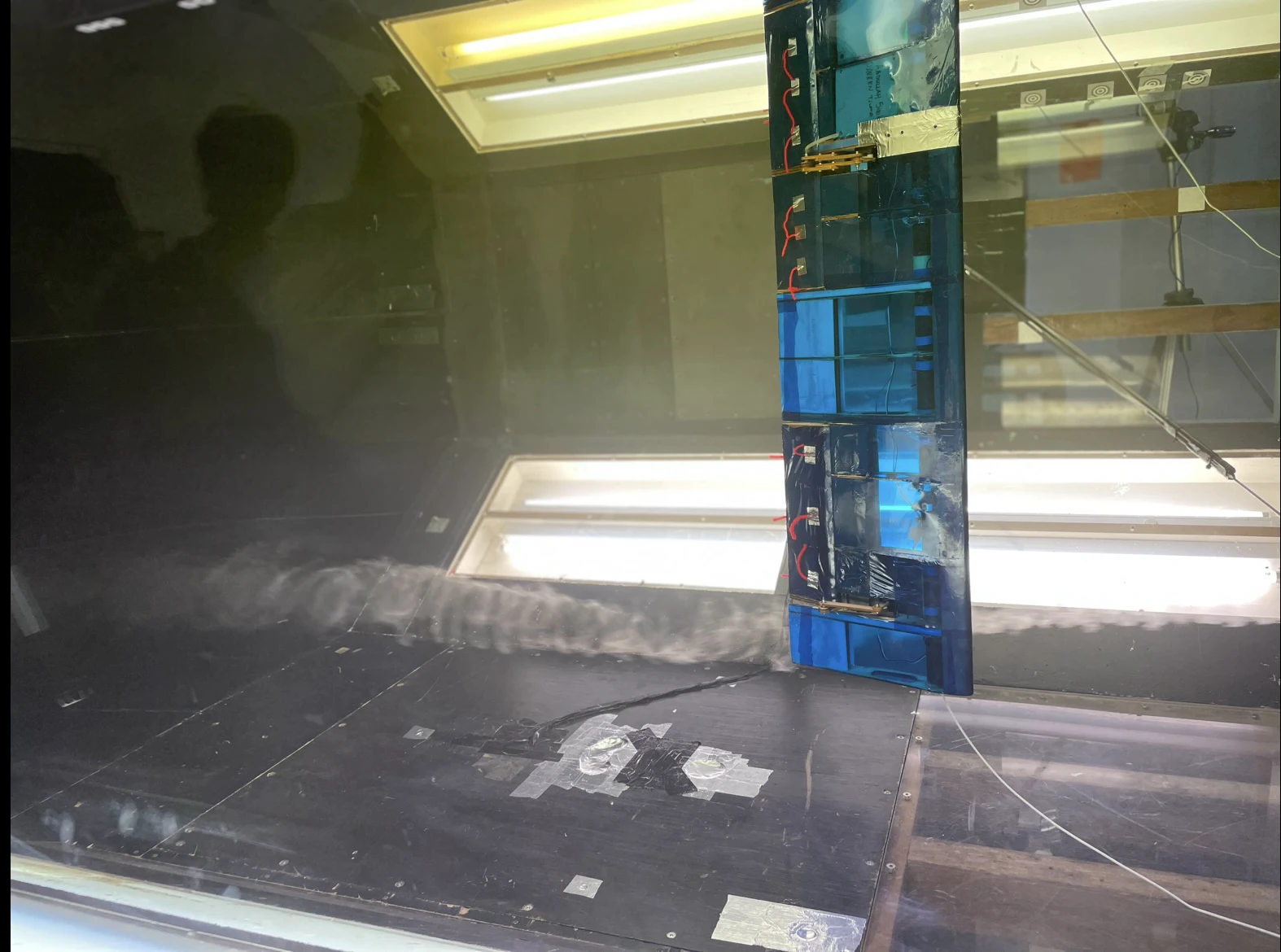 A dark frame from the tunnel camera stream showing the model in the test section with a bright streak of illuminated flow