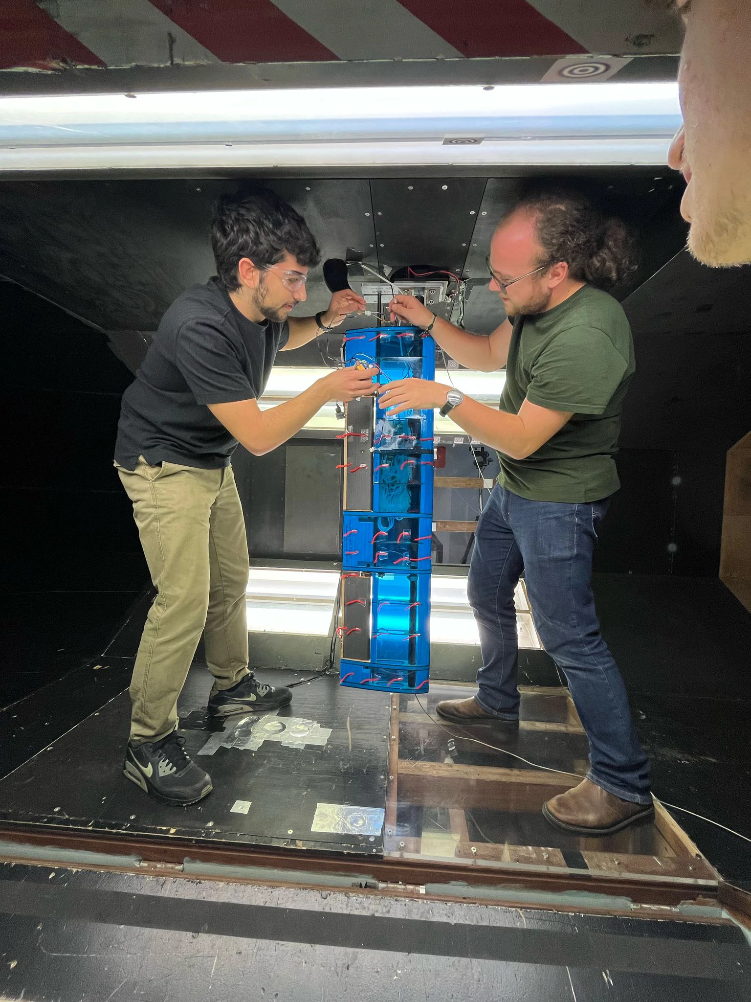 Two people inside the tunnel test section fitting the blue wing onto the mounting post